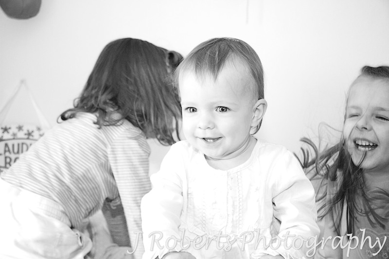Little girl laughing as her sisters bounce her on the bed - family portrait photography sydney